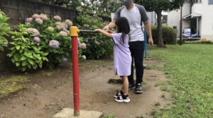 鉄棒の足抜き回りをする女の子を補助するお父さん