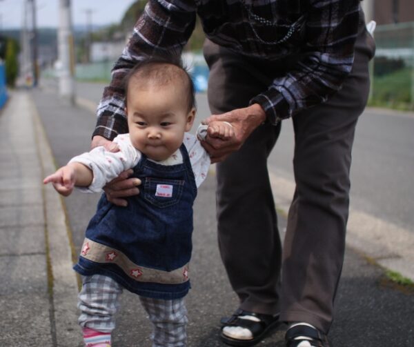 歩いている赤ちゃんの脇を支えているおじいちゃん