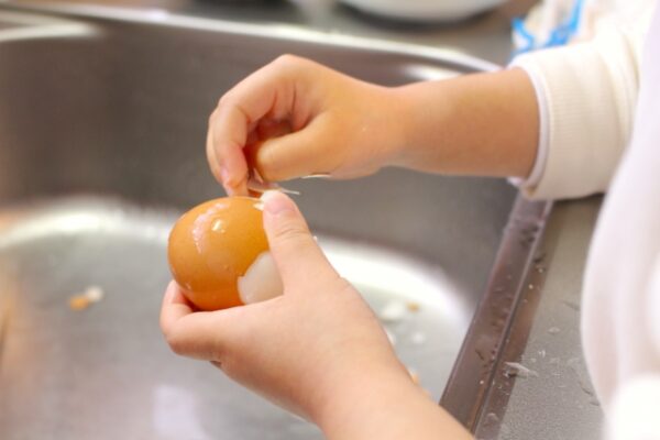 卵の殻をむいている子どもの手