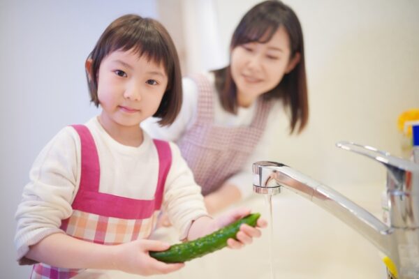 きゅうりを洗っている女の子と見ているお母さん