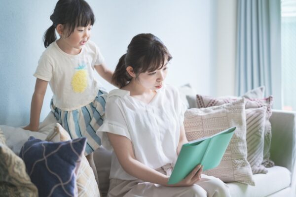 本を読んでいるお母さんとそれを後ろから見ている女の子